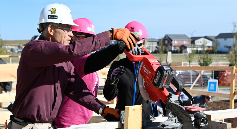 Andy shows two volunteers how to operate a mitre saw at Women Build.
