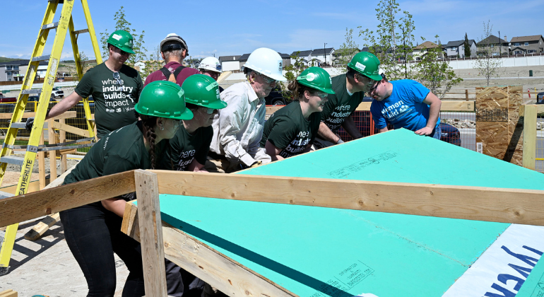 A group of volunteers stand shoulder to shoulder to lift a newly constructed exterior wall into place. 