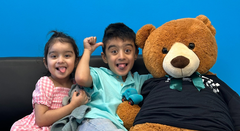 Zaviyar and Zarnish making silly faces beside a giant stuffed bear.