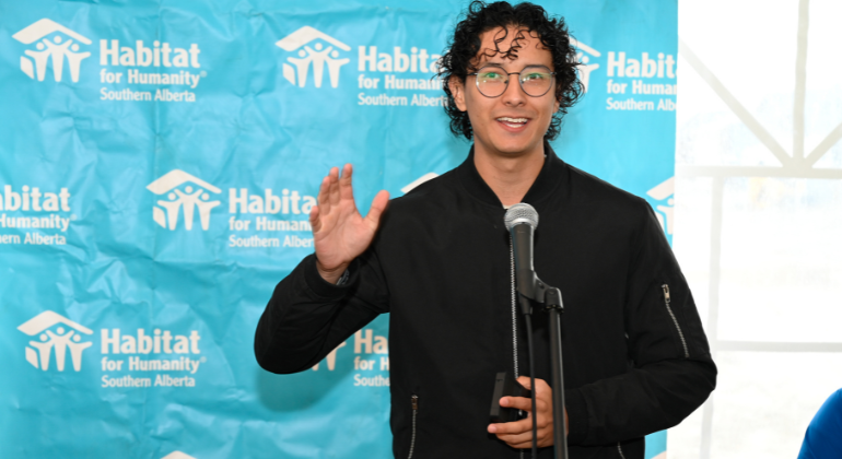 Santhiago, son of Habitat homeowner, stands in front of a Habitat sign while giving a speech to volunteers about the impacts of affordable homeownership on his life. 