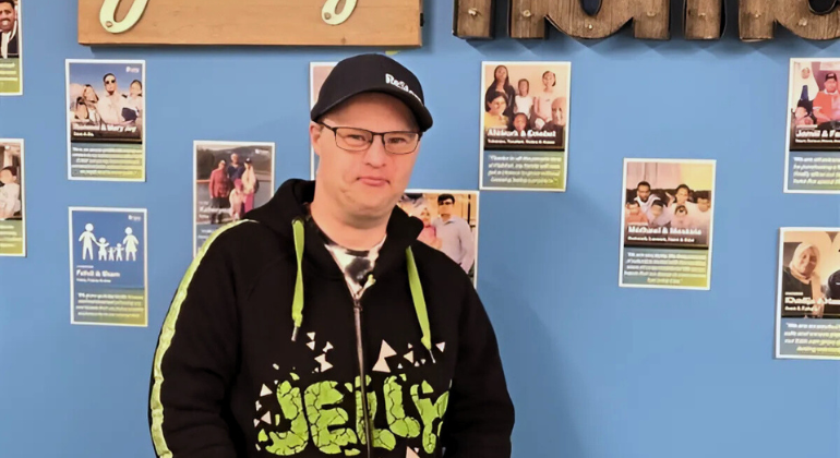 Jeffrey stands in front of a wall of Habitat family stories. 