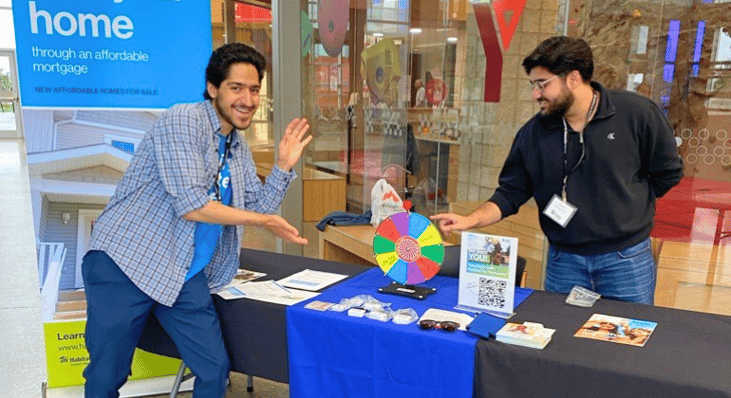 Two UCalgary volunteers enthusiastically showcasing the Habitat booth at a fair.