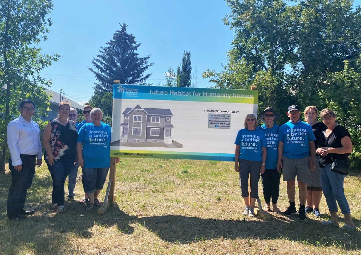 Habitat for Humanity Southern AB CEO stands alongside volunteers and donors at the unveiling of a large land sign announcing the future site of Habitat homes in High River
