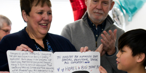 Marilyn Boake smiles proudly while accepting a handwritten thank you card from Habitat for Humanity homeowner's child