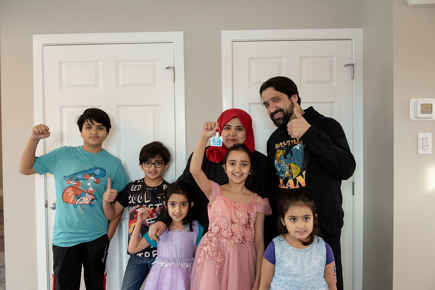 A family of seven celebrating getting the key to their new home by giving thumbs up and smiles at the camera