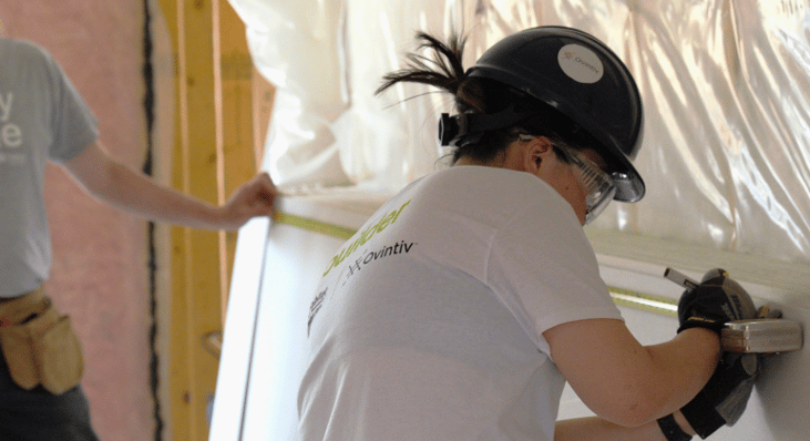 A woman measuring and marking a piece of drywall.