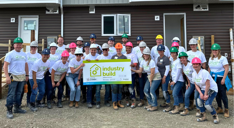 A group of volunteers holding an "Industry Build" sign in font of Habitat homes under construction