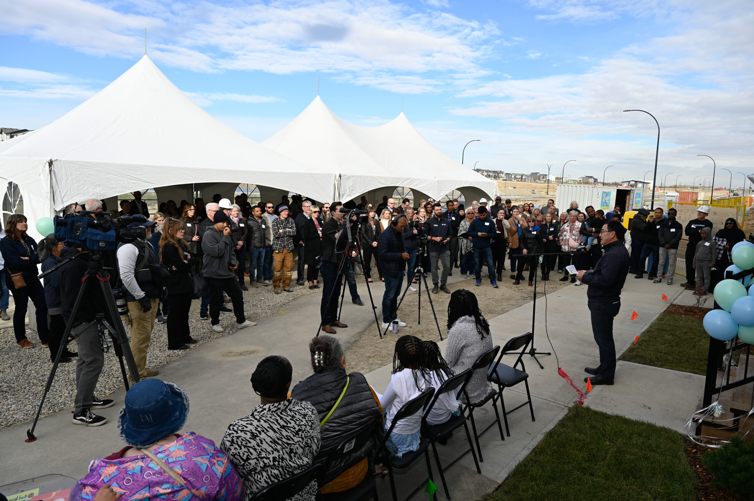 Media take photos and videos of a speaker in front of a Habitat townhome