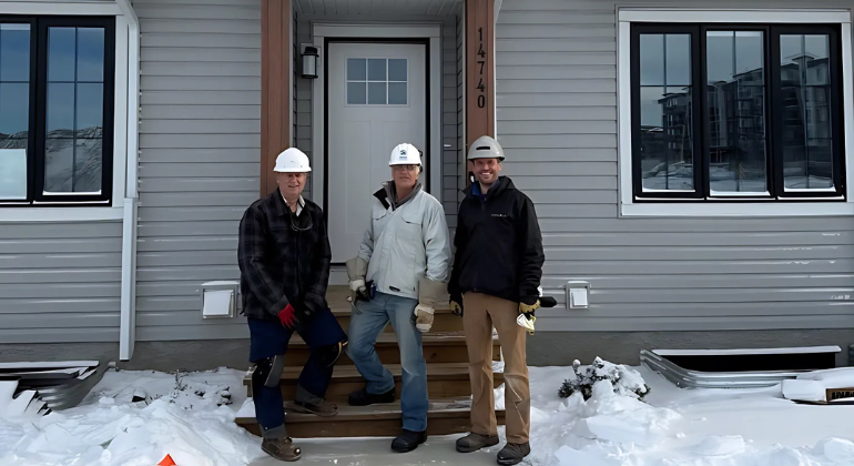 3 smiling men wearing hard hats in front of a Habitat townhome