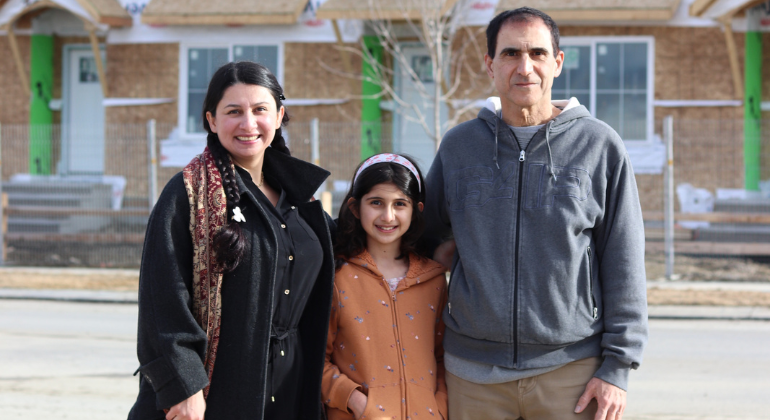 A family of three stand in front of their unfinished affordable home in Airdrie.