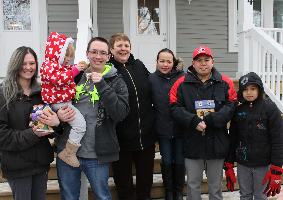 A woman stands with two Habitat families receiving the keys to their new homes.