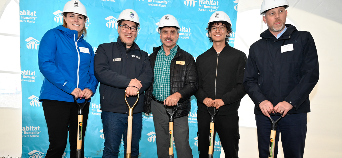 Five people wearing hard hats stand in front of a Habitat blue background holding ceremonial golden shovels