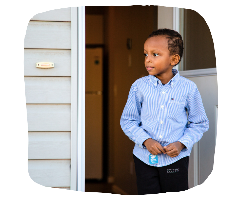 5 year old son of a Habitat homeowner stands in the doorframe of his new home.