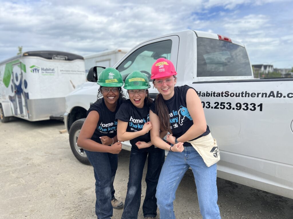Three girls wearing hard hats flexing their arm muscles