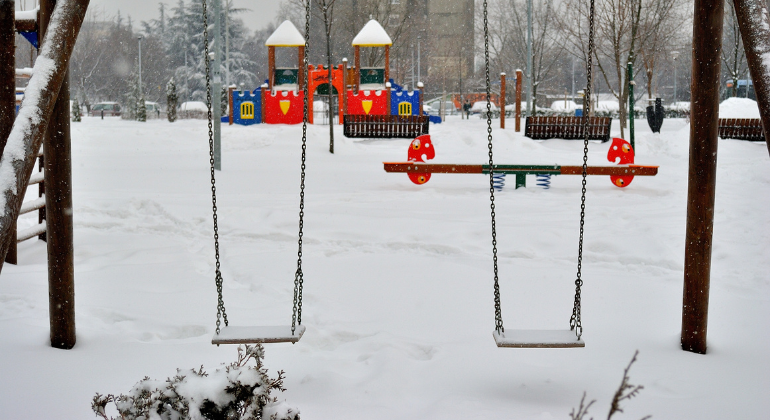 A snow-covered swing set in front of a playground in the winter