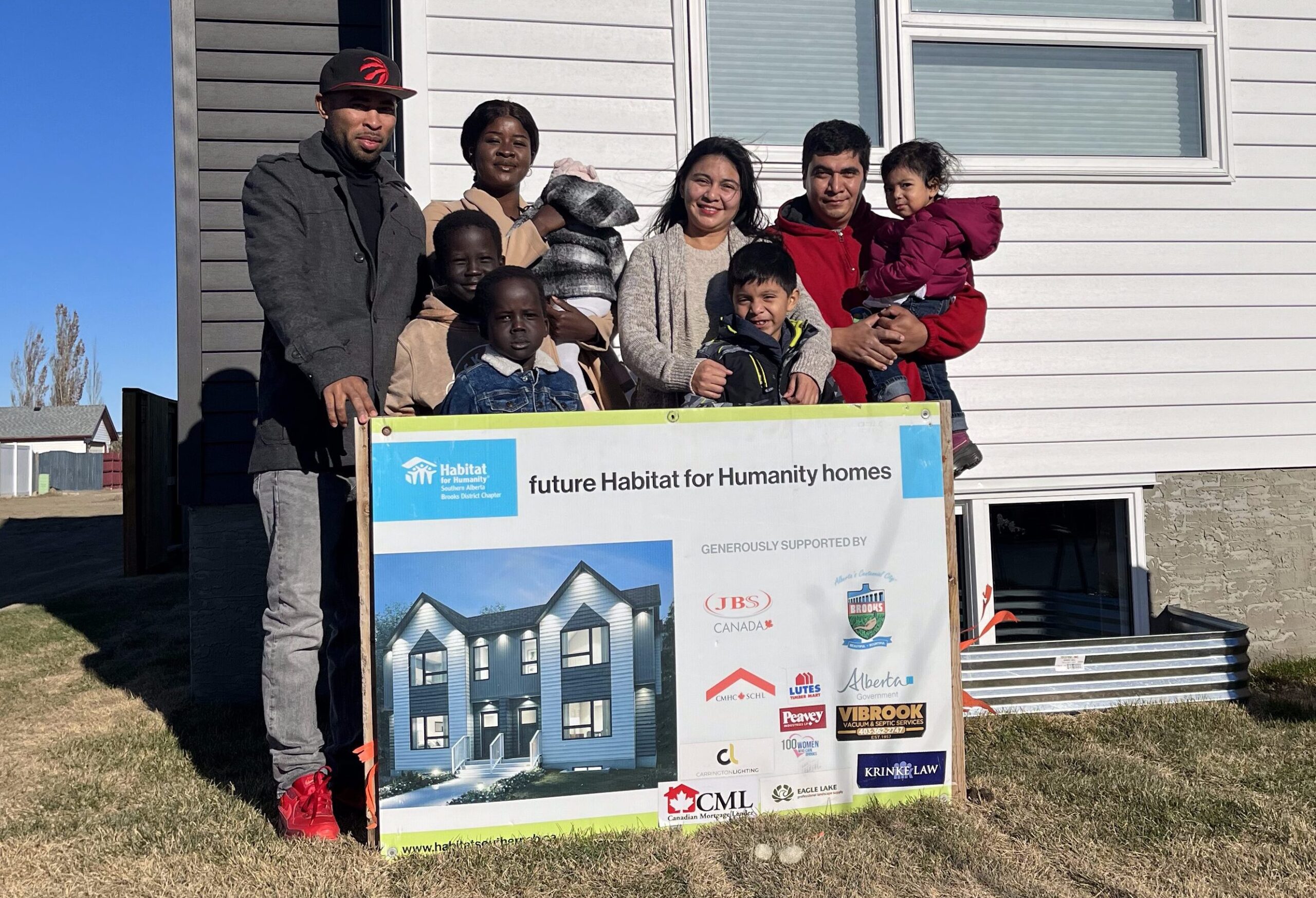 Two Habitat families in Brooks stand together in front of their new affordable homes.