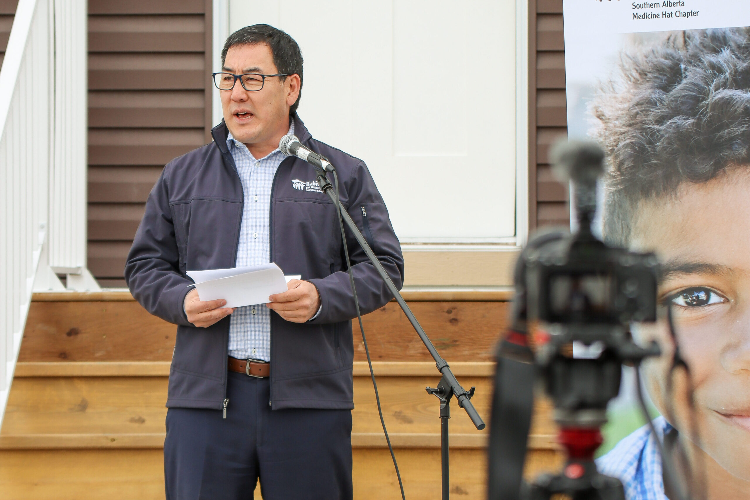 Gerrad gives a speech in front of finished homes while being filmed.