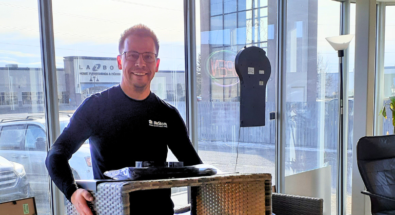 A smiling man holds a piece of wicker furniture on the ReStore sales floor