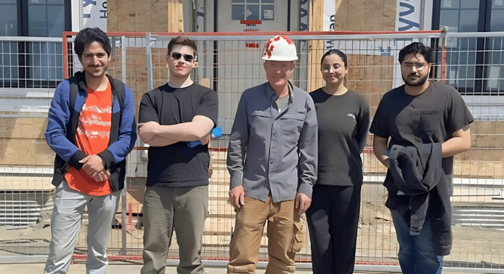 Four UCalgary volunteers stand with a Habitat staff in front of a Habitat build in Calgary.
