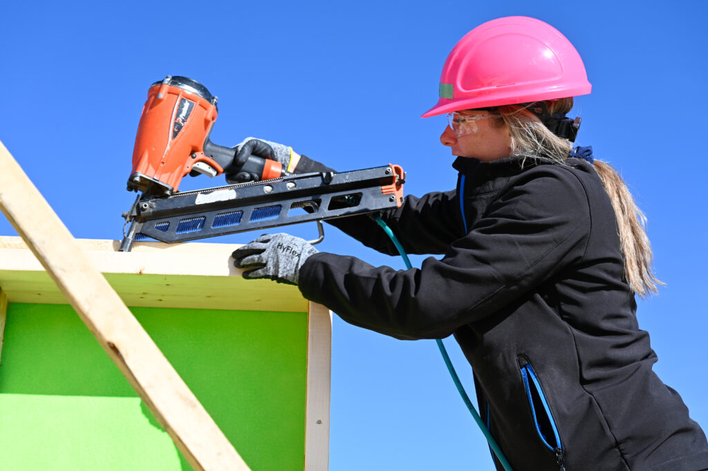Women wearing pink hardhat holding a nail gun