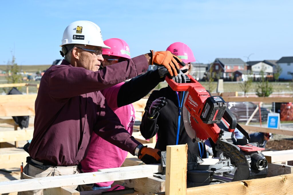 Volunteer Crew Leader Andy shows two volunteers how to operate a mitre saw.