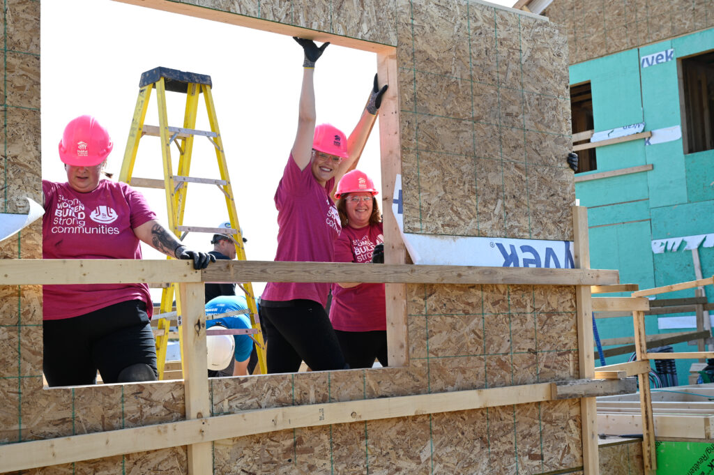 Three women on a construction site holding up a newly built wall
