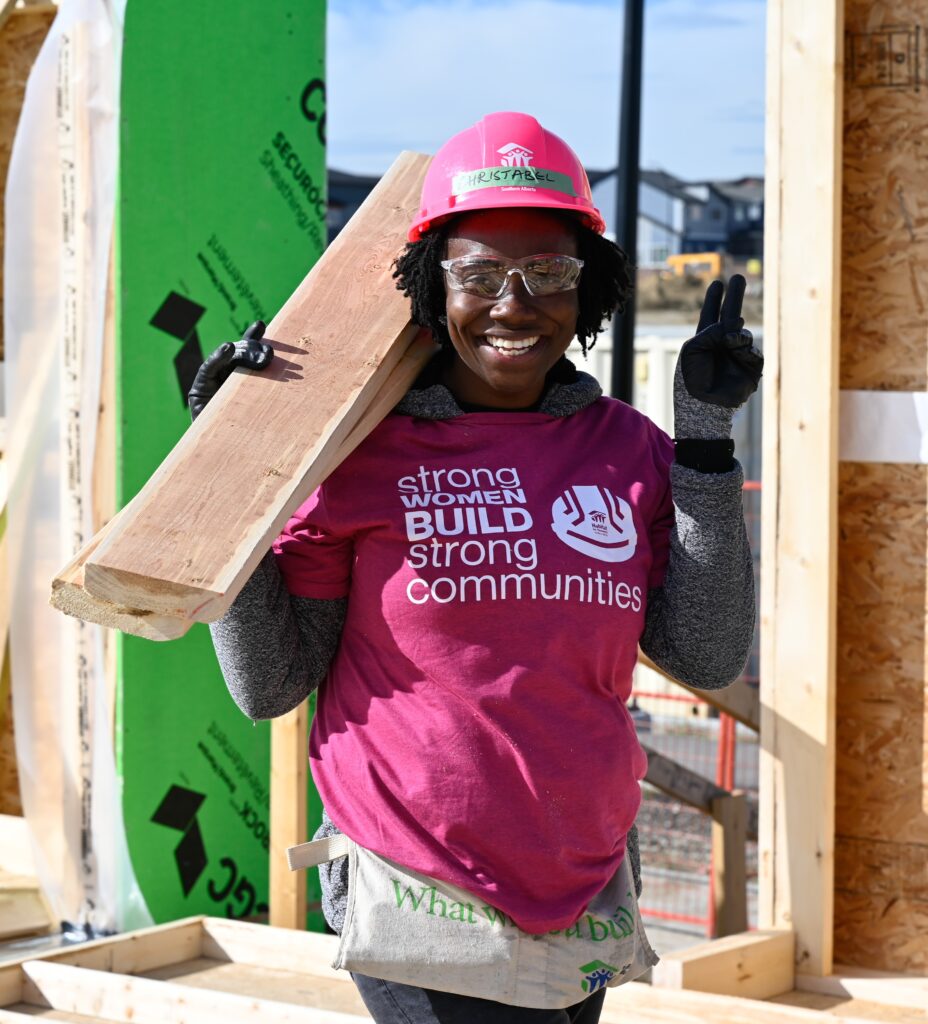 Women holding a plank of wood and holding up the peace sign to the camera