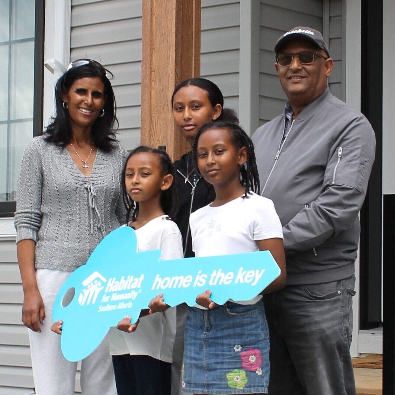 A family of five stands in front their home holding a giant key that says Home is the key.