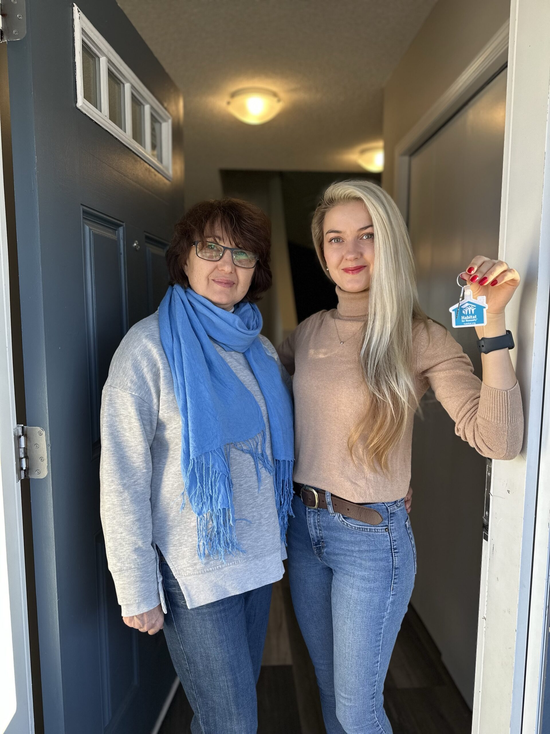 Kateryna, next to her mother, stands in the doorway of her affordable home in Calgary.