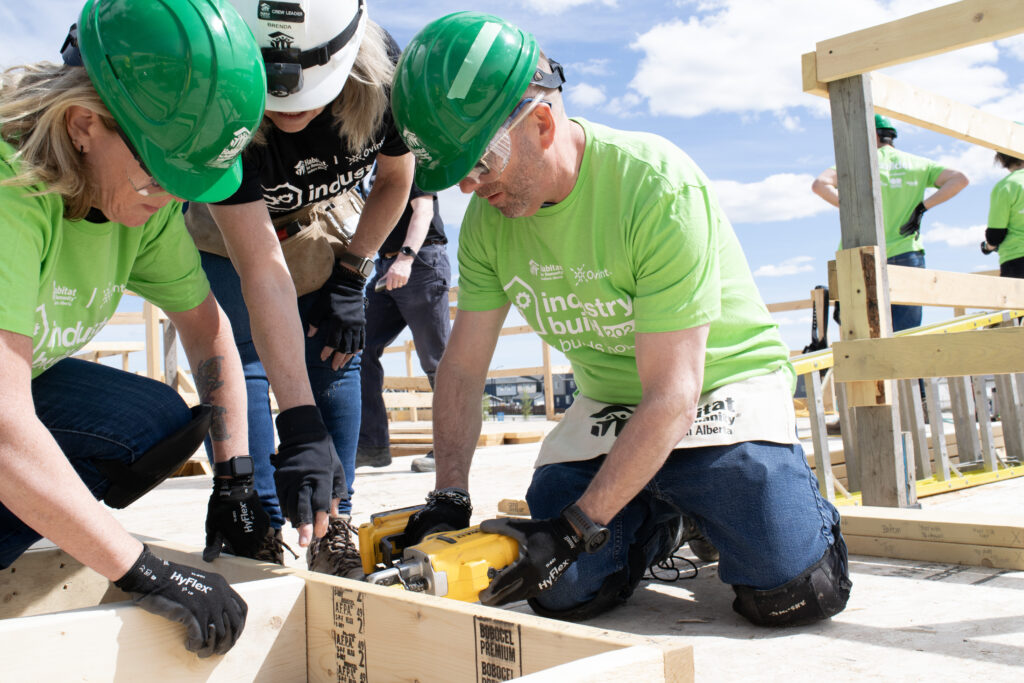 Three volunteers kneeling on the ground using a nail gun on a construction site