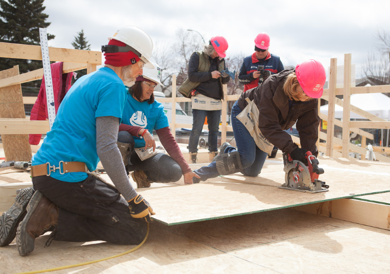 2 volunteers and a crew leader cut a piece of plywood with a circular saw