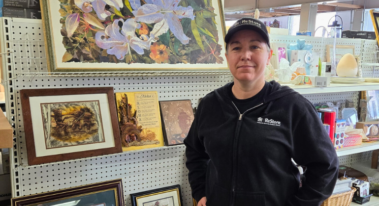 A woman in ReStore clothing stands in front of a shelf full of art pieces