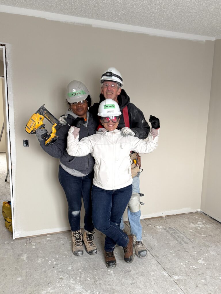 Three volunteers wearing hardhats posing with a nail gun