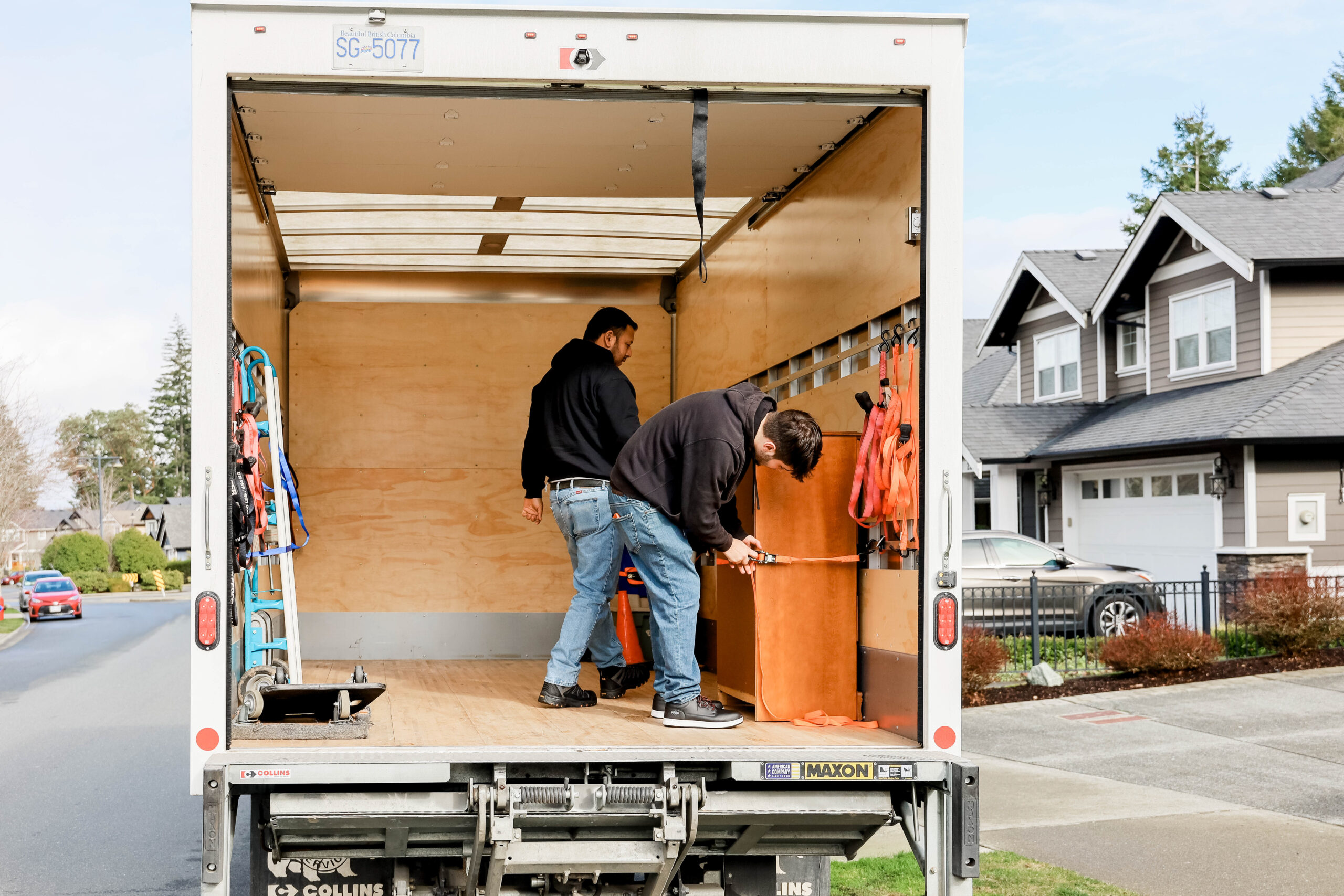 Two men secure a dresser in the back of a 1 ton truck. 