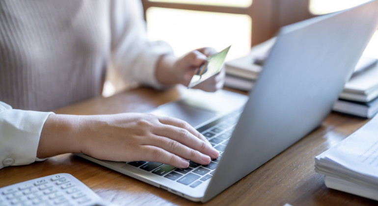 Close up showing a woman holding a credit card and using a laptop to shop online.