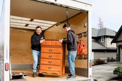 Two ReStore staff unload a donated dresser from a 1-ton truck.