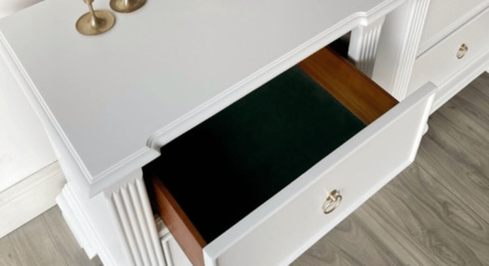 Close-up of one white nightstand with a half open drawer showing a dark green velvet lined drawer