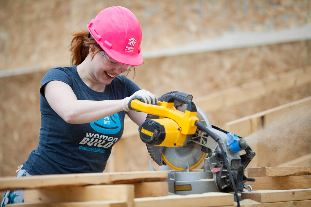 Women smiling while using power saw on a Habitat construction site