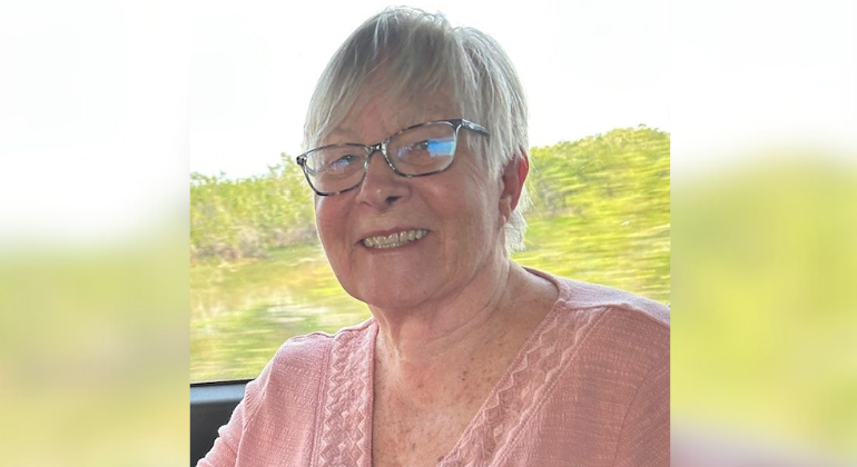 A smiling woman with a blurry green background, suggesting she is on a moving vehicle