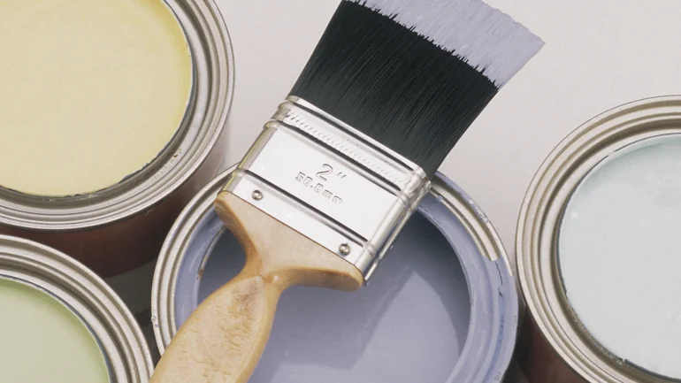 Paint brush rests on top of an open can of purple paint.