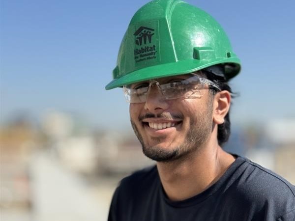 Close up of volunteer Rehman wearing a green Habitat branded hardhat.