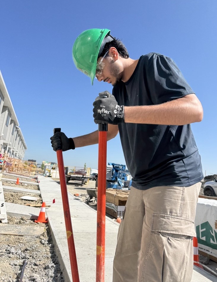 Volunteer Rehman dons a green hardhat as he digs postholes at a Habitat build site.
