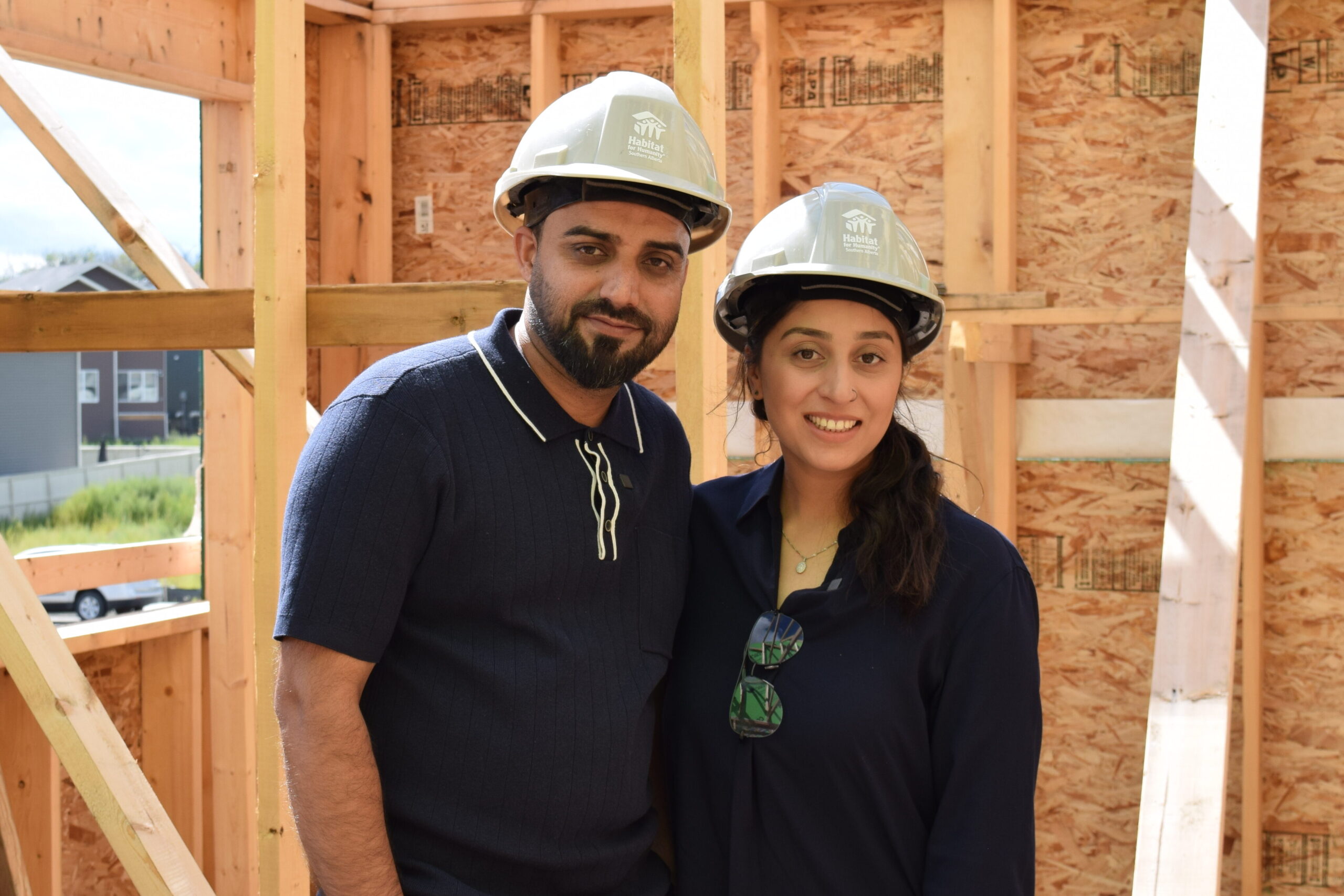 Habitat homeowners standing in their future bedroom wearing hardhats.