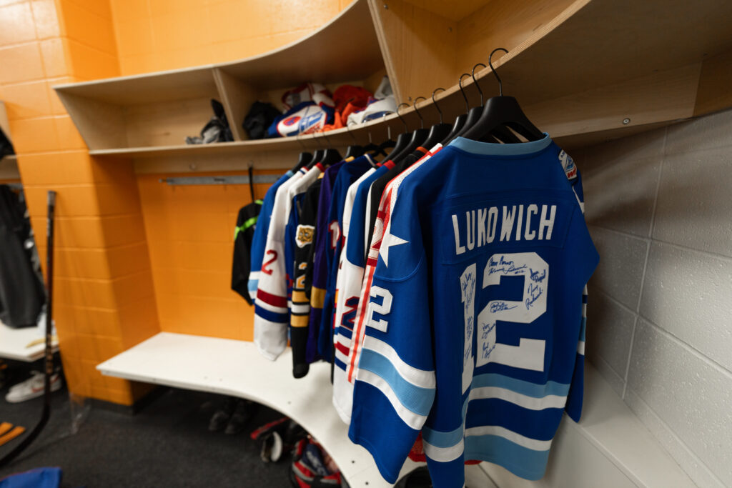 12 professional, autographed hockey jerseys hanging together in a dressing room at Hockey Helps the Homeless tournament in 2022.