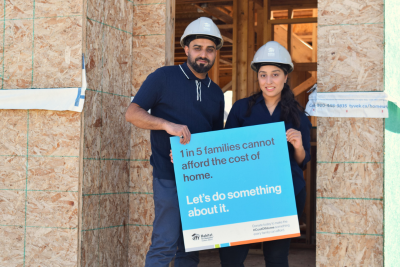 Homeowners Muhammed and Iqra hold a sign stating "I in 5 families cannot afford the cost of home. Let's do something about it."