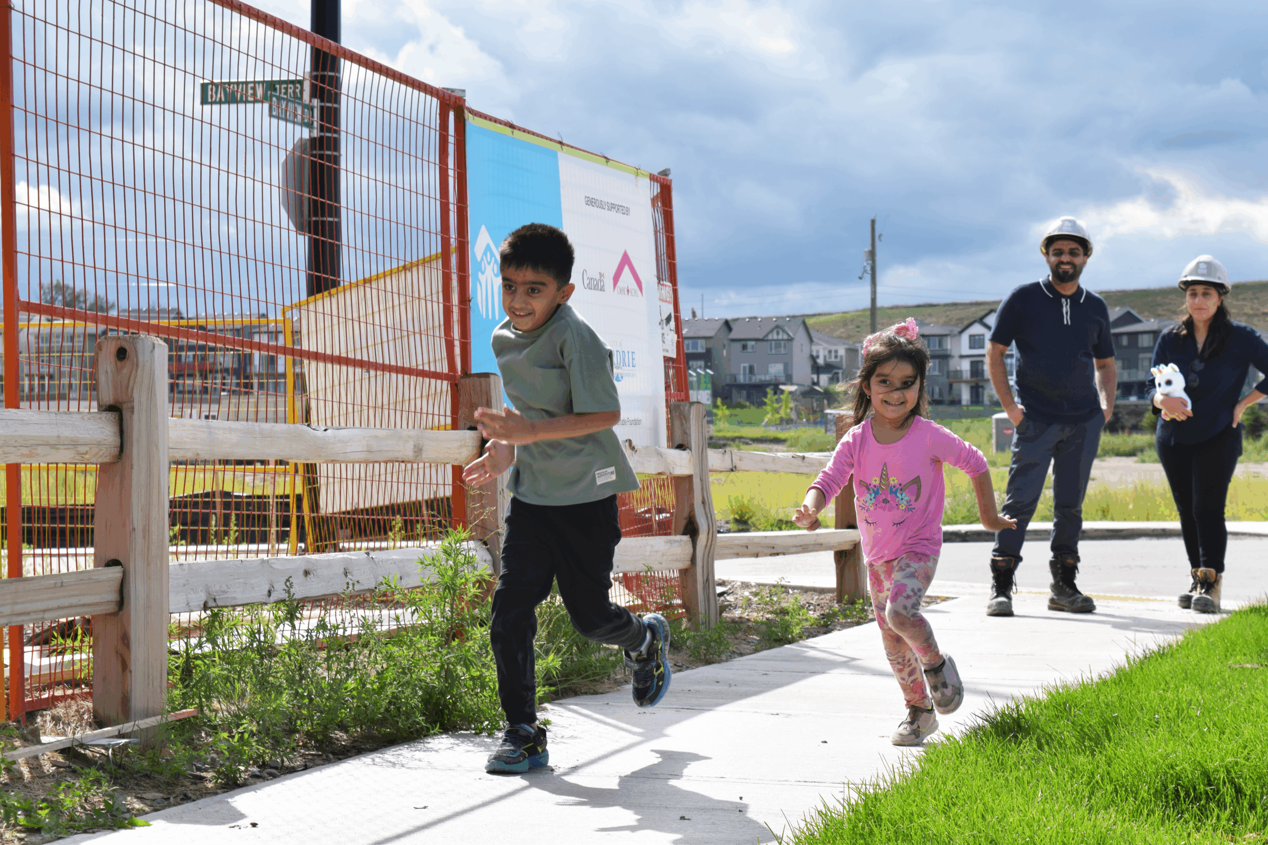 A habitat family running along the sidewalk in front of their future home