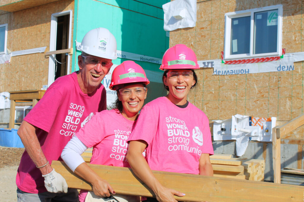 Three participants wearing hardhats carrying a piece of wood
