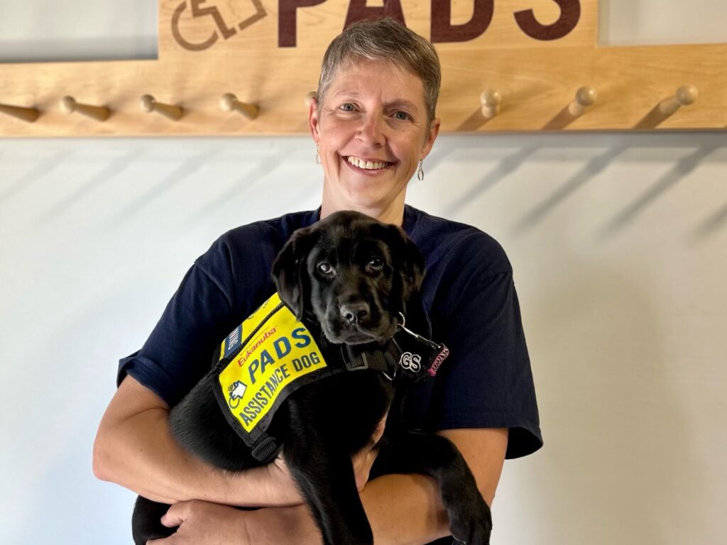 Habitat volunteer Bev holds a 10 week old black labrador retriever with a PADS vest.