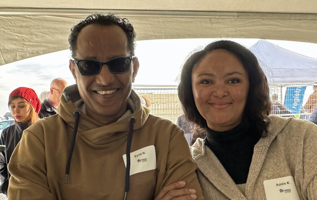 Addis and Eyob stand shoulder to shoulder under a white tent at a Habitat groundbreaking event. 