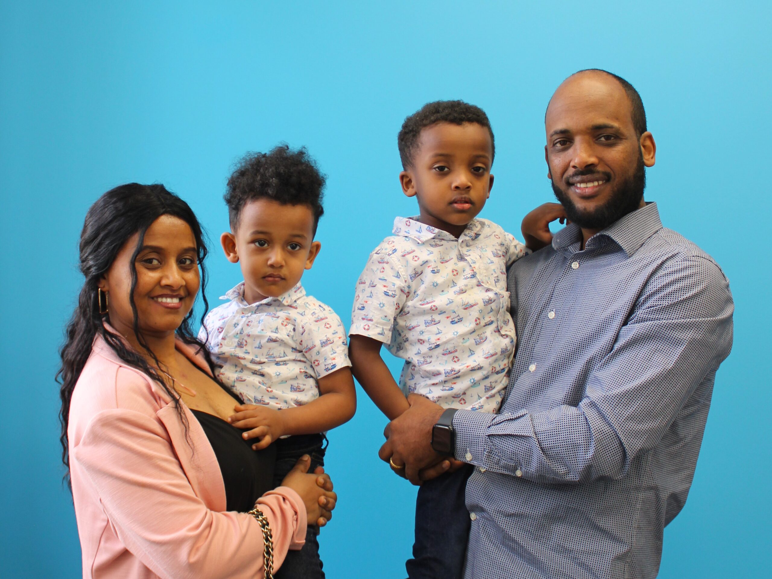 Tesfayesus and Wintana each hold one of their sons in front of a Habitat blue wall.